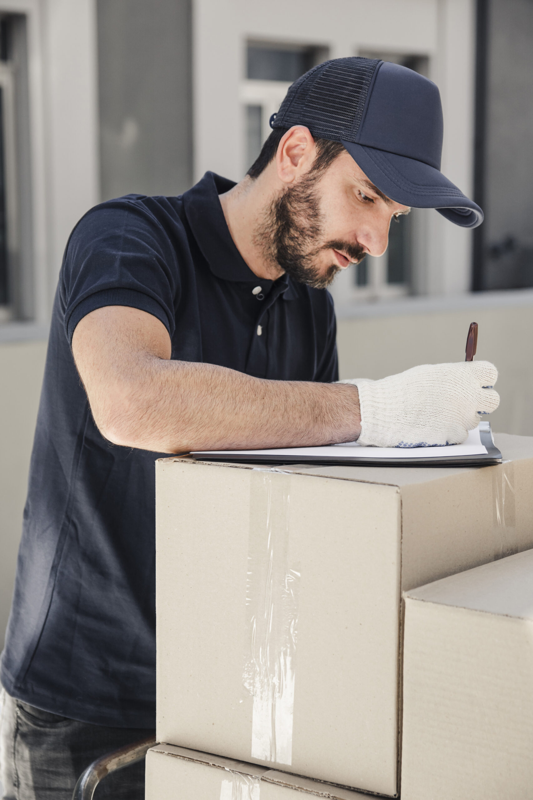 delivery-man-writing-clipboard-stacked-cardboard-boxes